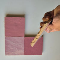 Hand holding a Peony Pink zellige tile showing the hand cut edge and natural terracotta clay body