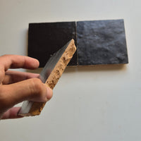 Hand holding a Matte Black zellige tile showing the hand cut edge and natural terracotta clay body